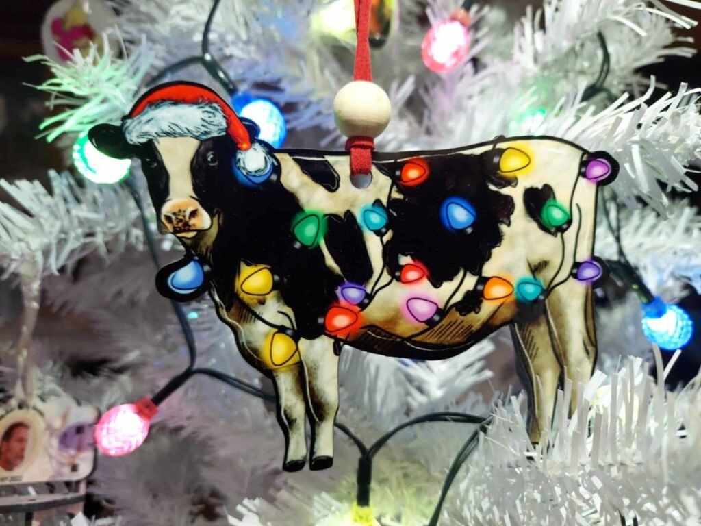 Appalachian Gifts, Graphic Tees & Personalized Tumblers 6 Black and white christmas cow ornament made from mdf. the cow is wearing a santa hat and is wrapped in christmas lights