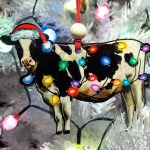 Black and white christmas cow ornament made from mdf. the cow is wearing a santa hat and is wrapped in christmas lights