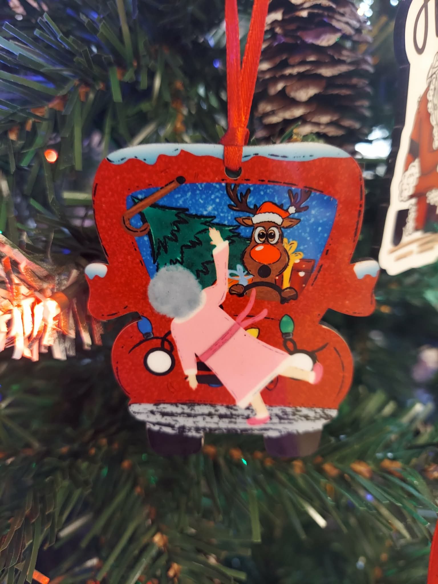 Grandma's Wild Ride Funny Christmas Ornament 1 Funny Christmas ornament of a startled reindeer in a Santa hat driving a red truck while grandma flies through the air in a pink robe