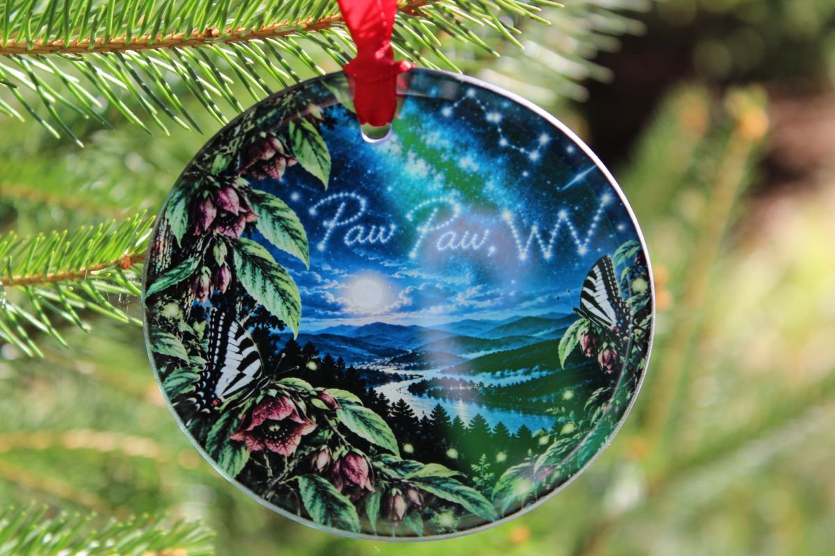 Paw Paw WV Ornament – Glass Hometown Keepsake 2 Paw Paw WV glass Christmas ornament with mountain and river artwork, pawpaw blossoms, and zebra swallowtail butterflies, hanging on a Christmas tree. Copy alt text