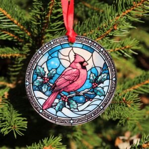 Red cardinal glass Christmas ornament with colorful faux stained-glass design and red hanging ribbon, displayed on a Christmas tree.